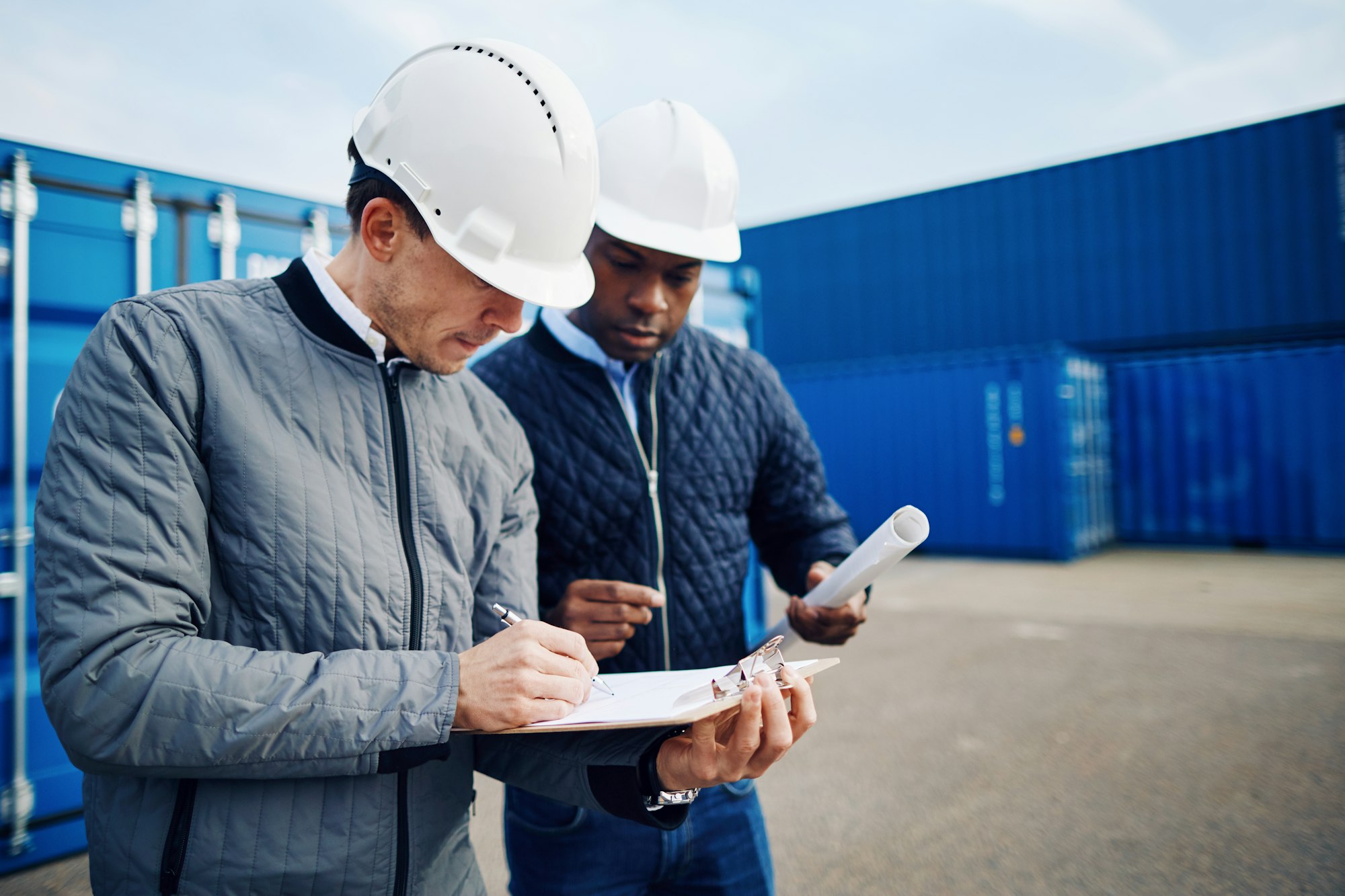 Two engineers standing in a shipping yard discussing logistics